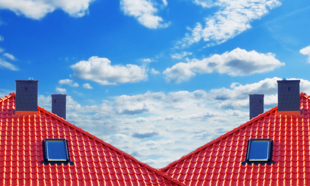 Red roof of new detached houses against blue sky.